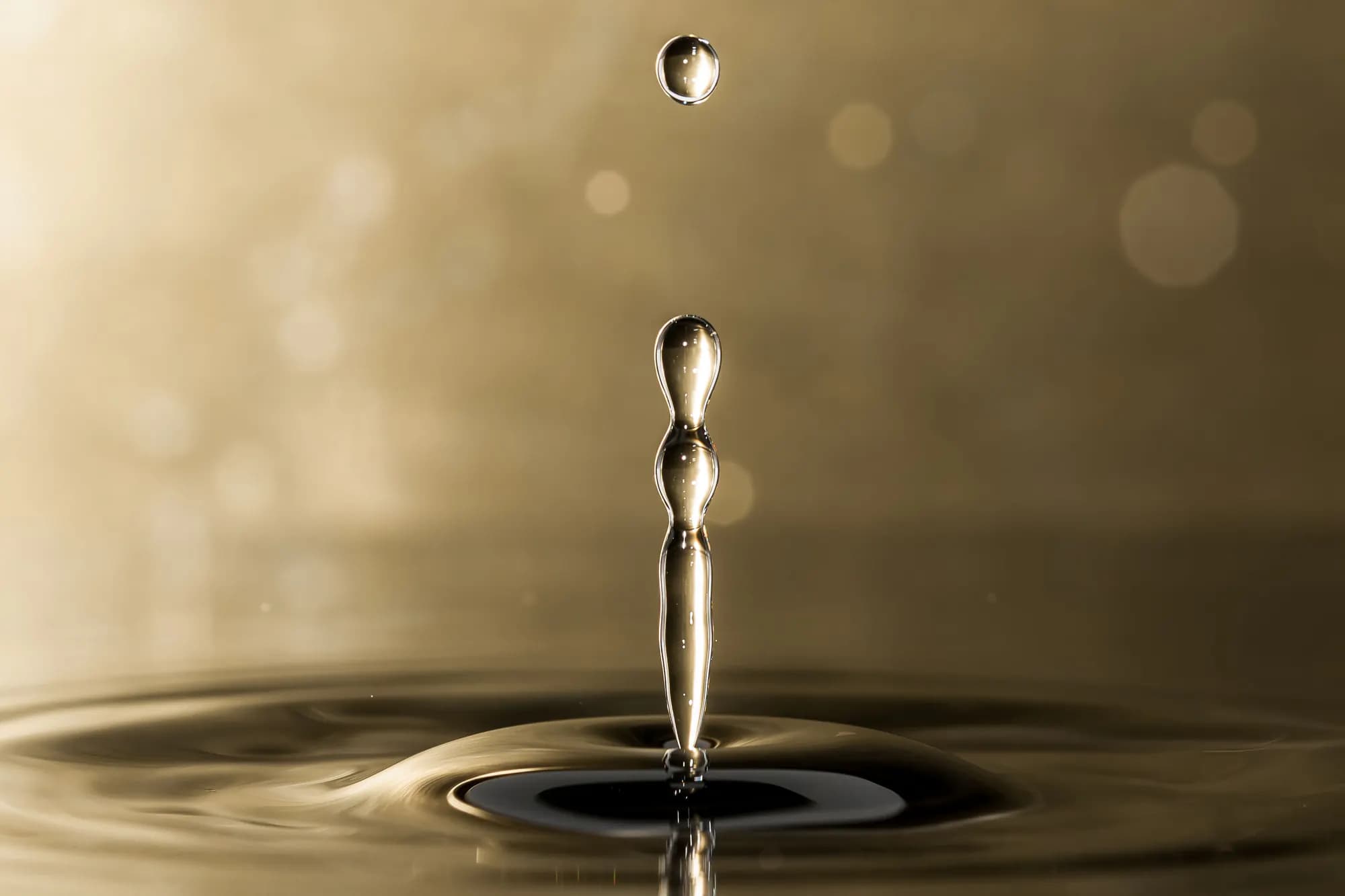Macro close-up of a golden droplet falling into a still pool of liquid